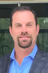 Professional headshot portrait of real estate agent Kenneth Roberts with a goatee, wearing a plaid grey suit jacket and a blue open-collared dress shirt.