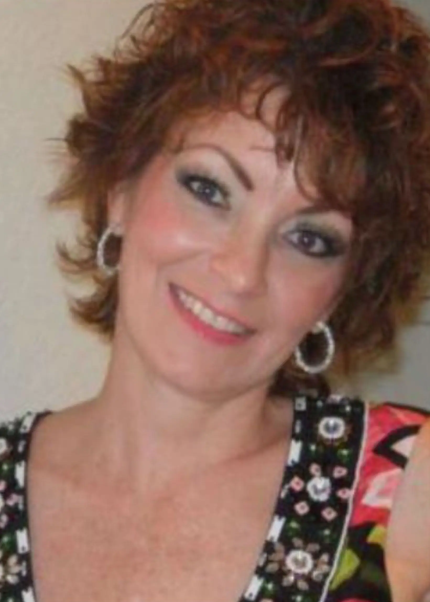 rofessional close-up headshot portrait of real estate agent Mindy LaCroix smiling, wearing a patterned sleeveless top and hoop earrings.