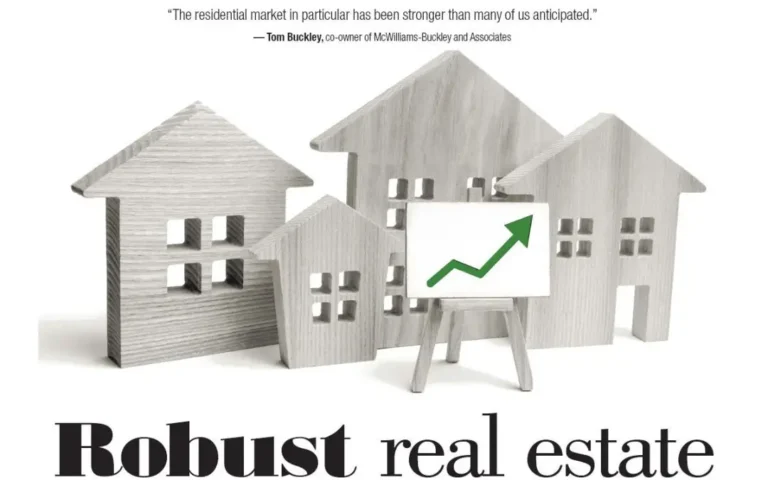 Graphic illustration showing miniature wooden model houses next to a whiteboard chart with an upward-trending green arrow, featuring a real estate market quote by Tom Buckley, co-owner of McWilliams Buckley and Associates.